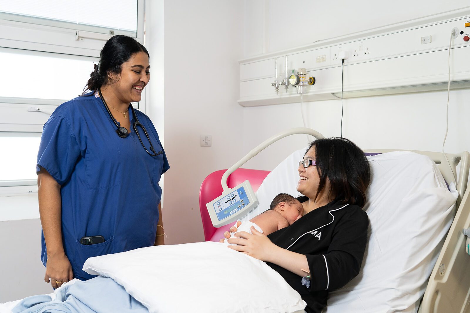 A midwife talking with a new mother and her baby on a postnatal ward